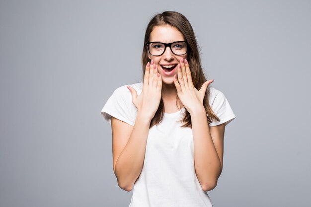 Young shy pretty lady in glasses in white t-shirt and blue jeans stay in front of white studio background