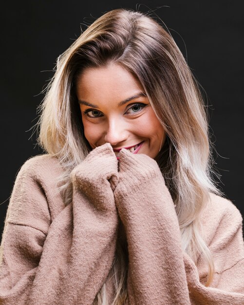 Young shy woman wearing sweatshirt posing against black wall