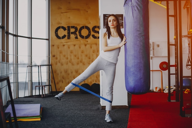 Young and skinny girl in a white shirt and gray leggings engaged in sports at the gym