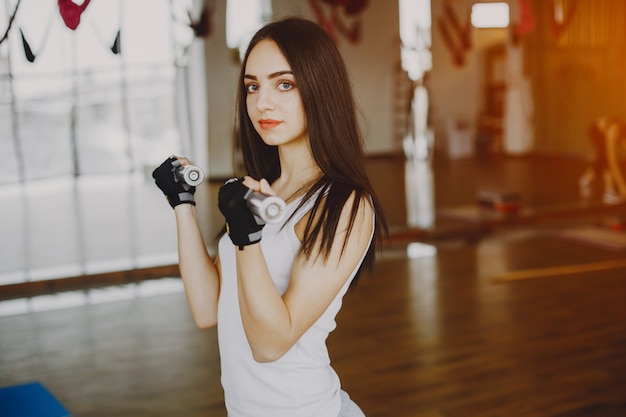 young and skinny girl in a white shirt and gray leggings engaged in sports at the gym