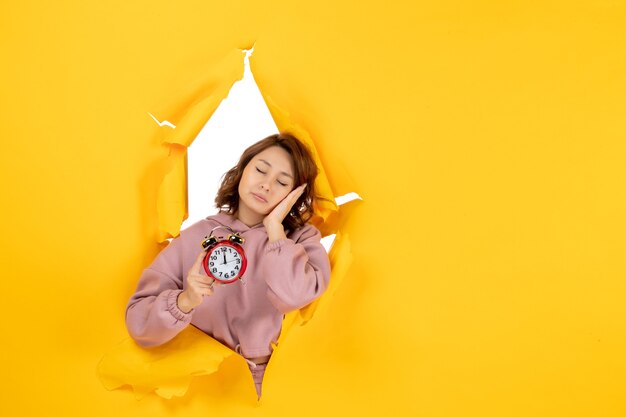 Young sleepy beautiful lady holding clock on yellow torn breakthrought background