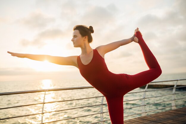 海、健康的なライフスタイルで日の出の朝にヨガをやっている若いスリムな美しい魅力的な女性