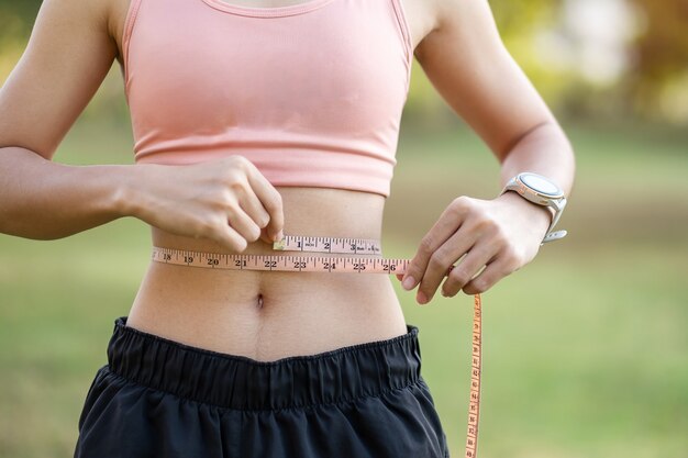ピンクのスポーツウェアの若いスリムな体の女性 彼女の細い腰を測定する健康な女性 プレミアム写真 ピンクのスポーツウェアの若いスリムな体の女性 彼女の細い腰を測定する健康な女性 プレミアム写真