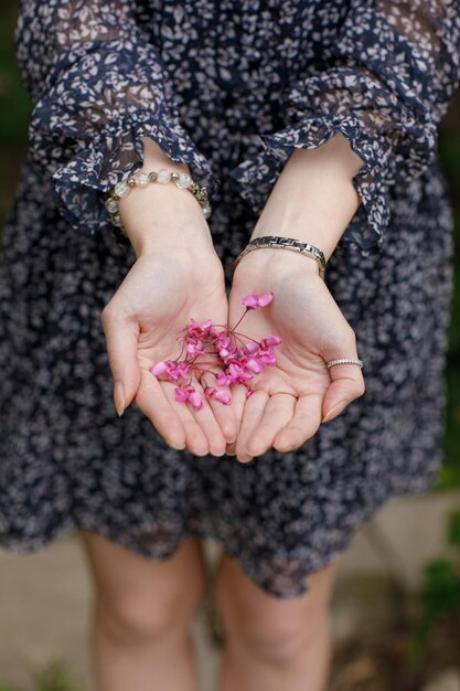 Young slim female standing holding blossom by hands in palms wearing stylish dress