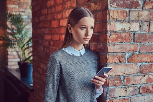 A young slim sensual girl in a gray dress leaning against a bric