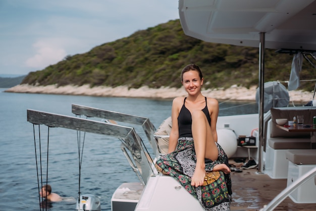 Young slim woman sitting in bikini bathing suit on a yacht and basking in the sun