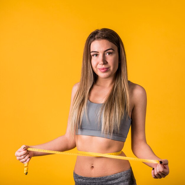 Young slim woman in sportswear measuring waist by tape