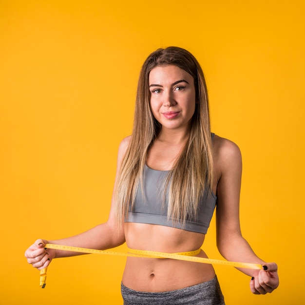 Young slim woman in sportswear measuring waist by tape