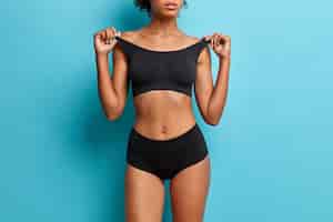 Бесплатное фото Молодая стройная женщина с здоровой кожей и плоским животом в черном укороченном топе и трусиках демонстрирует идеальное тело