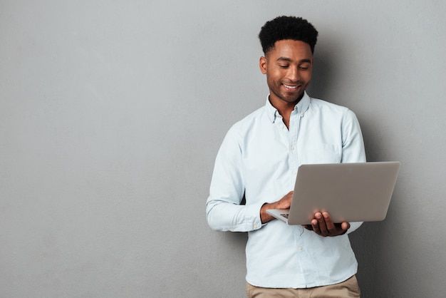 Young smiling african man standing and using laptop