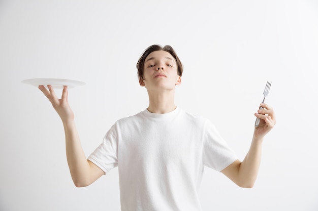 Free photo young smiling attractive caucasian guy holding empty dish and fork isolated on grey background. copy space and mock up. blank template background.