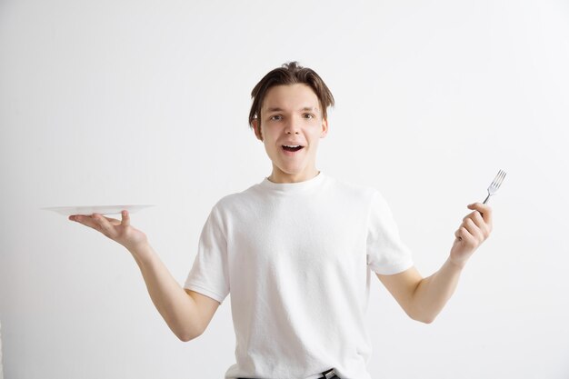 Young smiling attractive caucasian guy holding empty dish and fork isolated on grey