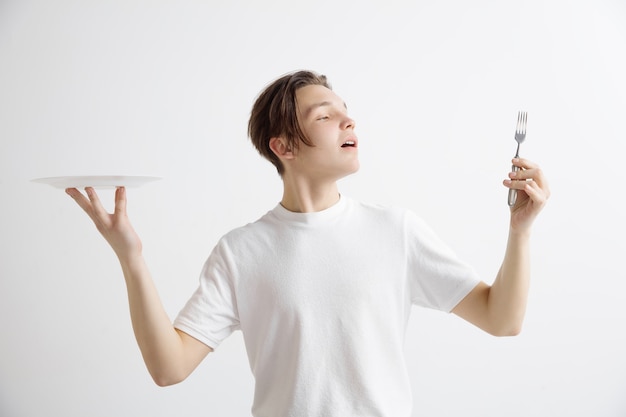 Free photo young smiling attractive caucasian guy holding empty dish and fork isolated on grey