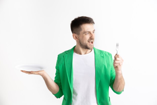 Young smiling attractive caucasian guy holding empty dish and fork isolated on grey