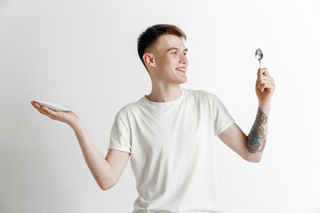 Young smiling attractive guy holding empty dish and fork isolated on grey wall.