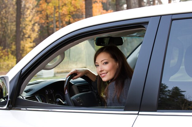 若い笑顔の美しい女性が新しい車に座っています
