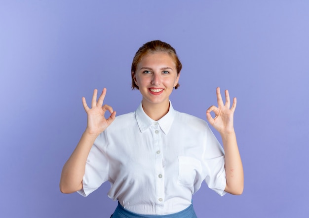 Giovane ragazza russa bionda sorridente gesti il segno giusto della mano con due mani isolate su fondo viola con lo spazio della copia