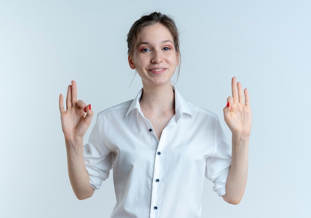 Young smiling blonde russian girl gestures ok hand sign with two hands isolated on white space with copy space