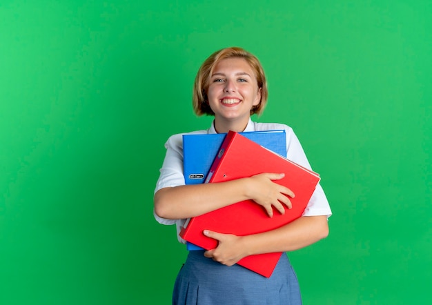 Young smiling blonde russian girl holds file folders isolated on green background with copy space