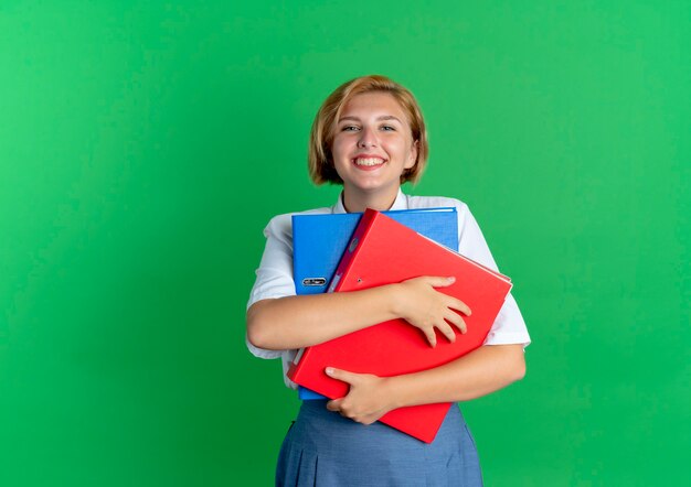 若い笑顔の金髪のロシアの女の子は、コピースペースで緑の背景に分離されたファイルフォルダを保持