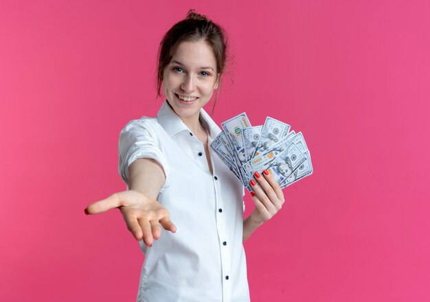 若い笑顔のブロンドのロシアの女の子は、コピースペースでピンクに手を差し伸べてお金を保持します