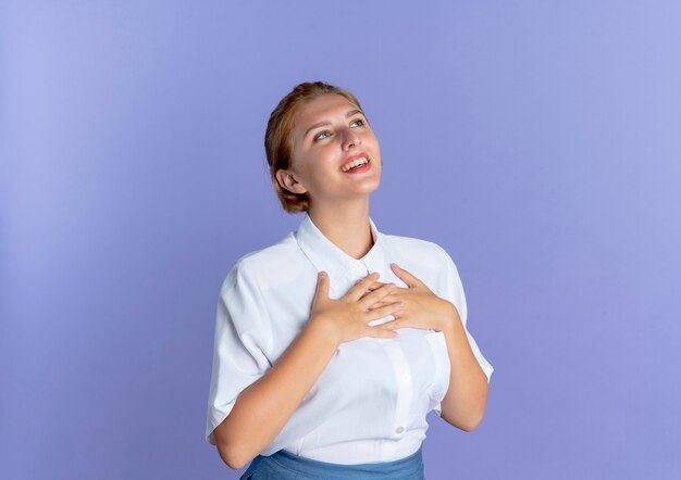 young smiling blonde russian girl puts hands on chest looking up