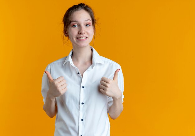 Young smiling blonde russian girl thumbs up isolated on orange space with copy space