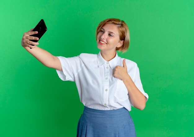 young smiling blonde russian girl thumbs up looking at phone