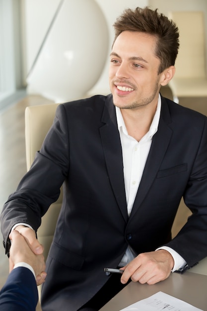 Young smiling businessman shaking male hand at meeting, first im