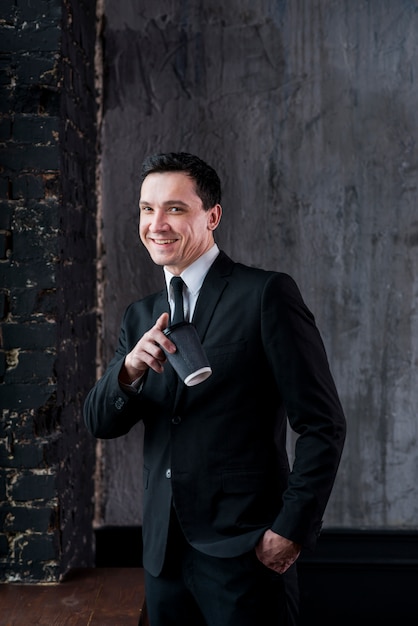 Young smiling businessman with coffee cup pointing at camera