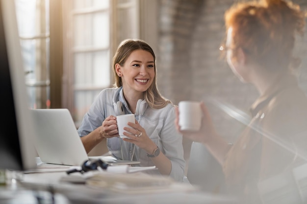 Free photo young smiling businesswoman and her female colleague communicating while having coffee break in the office