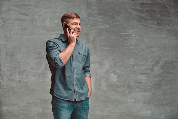 The young smiling caucasian businessman on gray space talking with phone