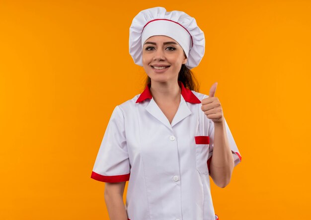 요리사 유니폼 엄지 손가락에 젊은 웃는 백인 요리사 소녀 복사 공간 오렌지 벽에 고립