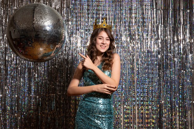 Young smiling charming lady wearing blue green shiny dress with sequins with crown in the party