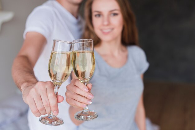 Молодая пара улыбаясь, лязгая бокалами шампанского в домашних условиях