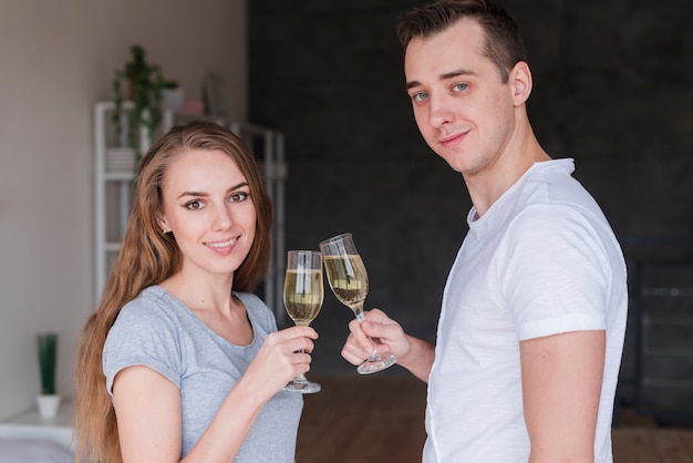 若い笑顔のカップルが自宅で飲み物のグラスを交換