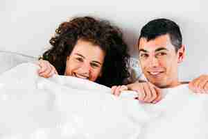 Free photo young smiling couple under duvet
