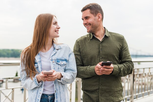 Young smiling couple holding cellphone looking at each other