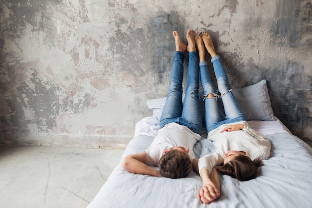 Free photo young smiling couple lying on bed at home in casual outfit