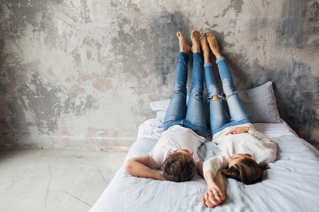 Young smiling couple lying on bed at home in casual outfit