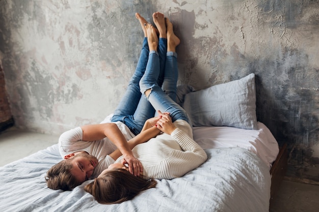 Молодая улыбающаяся пара, лежа на кровати дома в повседневной одежде