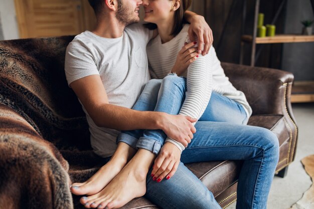 Young smiling couple sitting on couch at home in casual outfit, love and romance, woman and man embracing, wearing jeans, spending relaxing time together