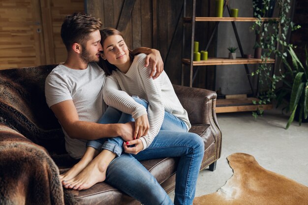 Young smiling couple sitting on couch at home in casual outfit