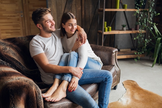 Young smiling couple sitting on couch at home in casual outfit