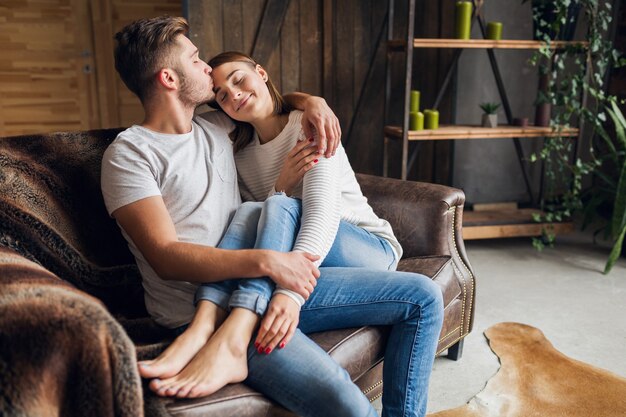 Young smiling couple sitting on couch at home in casual outfit