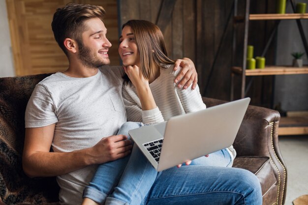 Young smiling couple sitting on couch at home in casual outfit