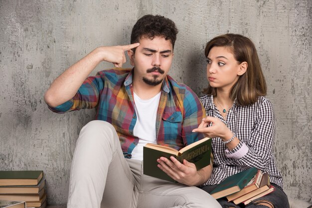 young smiling couple sitting on the floor with books