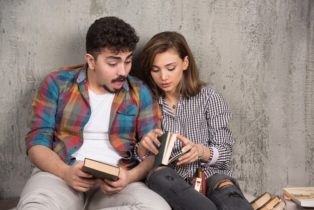 young smiling couple sitting on the floor with books