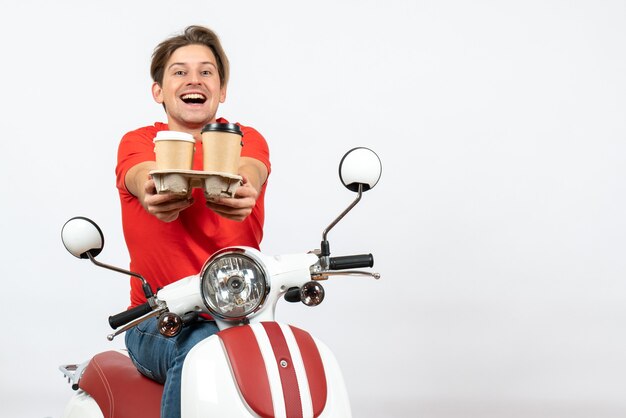 Young smiling courier man in red uniform sitting on scooter and giving orders on yellow wall