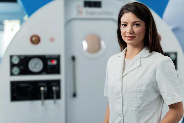 Young smiling doctor standing by hyperbaric chamber at clinic and looking at camera